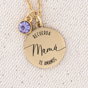 May include: Gold necklace with a round pendant that says "Recuerda Mam&aacute; Te Amamos" in black lettering. The pendant has a small purple gemstone attached to the top.