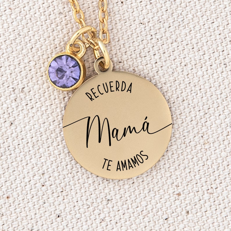 May include: Gold necklace with a round pendant that says "Recuerda Mam&aacute; Te Amamos" in black lettering. The pendant has a small purple gemstone attached to the top.