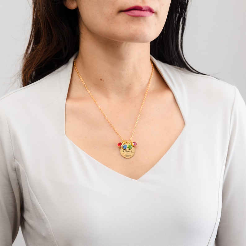 May include: Gold necklace with a round pendant that says "Mama" in cursive. The pendant has four small colorful gemstones attached to it.