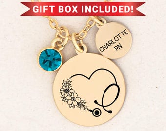May include: Gold-colored necklace with a pendant featuring a heart-shaped design with a stethoscope and floral accents. Includes a teal-colored gemstone and a round charm engraved with "CHARLOTTE RN". The text "GIFT BOX INCLUDED!" is displayed.