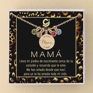 May include: A gold necklace with a round charm that says "Recuerda Mam&aacute; Te Amamos" in Spanish. The necklace has five colorful crystal charms. The necklace is in a white box with a leopard print background.