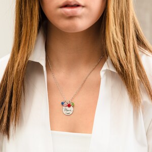 May include: A silver necklace with a round pendant that says "Maman" with a small heart and the words "31 ann&eacute;es" on it. The pendant has five small colorful gemstones attached to it.