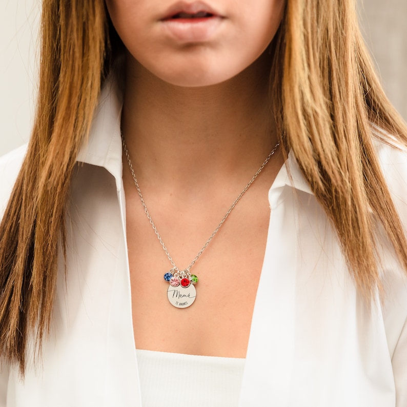 May include: A silver necklace with a round pendant that says "Maman" with a small heart and the words "31 ann&eacute;es" on it. The pendant has five small colorful gemstones attached to it.