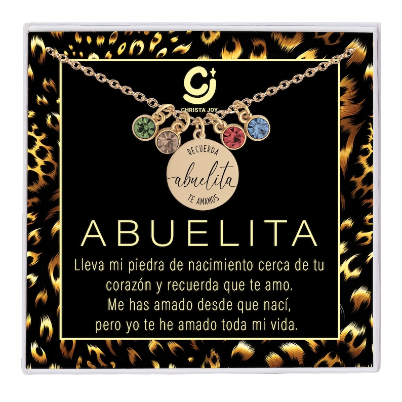 May include: A gold necklace with a charm that says "Recuerda abuelita te amamos" and a variety of colored crystals. The necklace is displayed in a black box with a leopard print background. The text "Abuelita" is written in large letters below the charm.