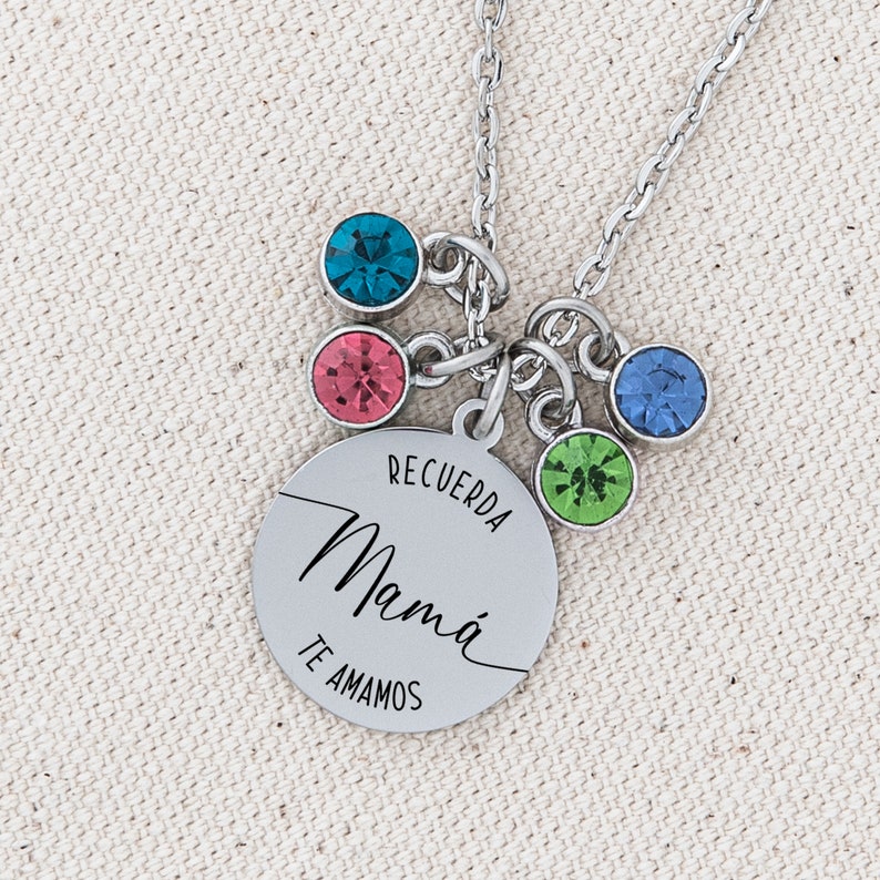 May include: Silver necklace with a round charm that says "Recuerda Mam&aacute; Te Amamos". The charm has five colorful crystals attached to it.