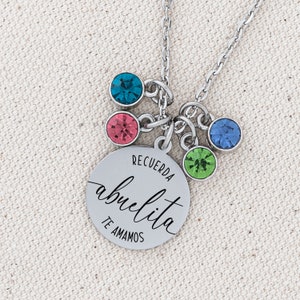 May include: A silver necklace with a round charm that says "Recuerda abuelita te amamos". The charm has five small colorful crystals attached to it.