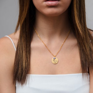 May include: A gold necklace with a round pendant that says "Mama" in cursive. The pendant has a small blue gemstone on top.