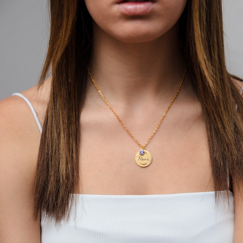 May include: A gold necklace with a round pendant that says "Mama" in cursive. The pendant has a small blue gemstone on top.
