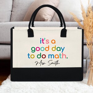 Op de afbeelding: Een canvas draagtas met zwarte handvatten en een zwart onderste paneel. De tas heeft de tekst "it's a good day to do math" in kleurrijke letters, met "Mrs. Smith" in een handschrift eronder.