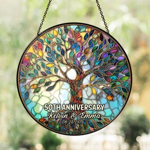 May include: A round, stained-glass window featuring a colorful tree design. The tree has a brown trunk and branches with leaves in shades of green, blue, yellow, and purple. The text "50TH ANNIVERSARY Kelvin & Emma 06.25.1975" is displayed.