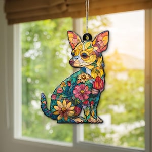 May include: A colorful Chihuahua ornament with a stained-glass effect. The dog is adorned with floral patterns in shades of yellow, orange, pink, and blue. It hangs from a silver chain, perfect for a window or rearview mirror.