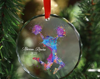 May include: A clear, round glass Christmas ornament with a red ribbon. The ornament features a colorful watercolor design of a cheerleader in mid-jump, with the name "Marian Rivera" and the year "2025" printed on it.