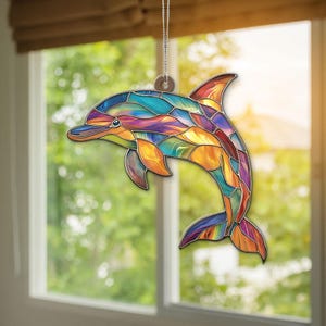 Op de afbeelding: Een Delfin-ornament van gekleurd glas met een kleurrijk ontwerp in blauw, paars, geel en rood. De dolfijn springt uit het water.