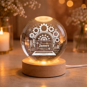 May include: A clear glass sphere lamp featuring an internal 3D laser-etched design of a laptop with the name James displayed on the screen, surrounded by mechanical gears and technical grid patterns, resting on a circular light-up wooden base.