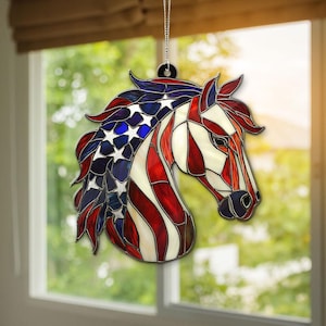 Könnte beinhalten: Ein Glasmalerei-Pferdekopf-Ornament mit patriotischem Design. Die Mähne und ein Teil des Kopfes des Pferdes weisen einen blauen Hintergrund mit weißen Sternen auf, während der Rest des Kopfes rote und weiße Streifen aufweist. Es hängt an einer silbernen Kette.