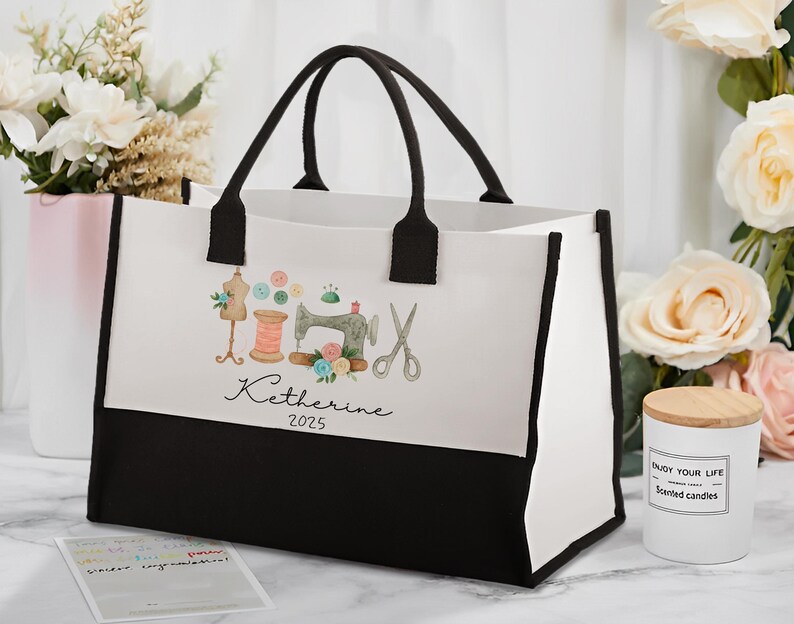 Peut inclure: Un sac fourre-tout blanc avec des bordures et des poign&eacute;es noires. Le sac pr&eacute;sente un motif aquarelle d'outils de couture, dont une machine &agrave; coudre, des ciseaux et du fil. Le nom "Katherine" et l'ann&eacute;e "2025" sont &eacute;galement imprim&eacute;s sur le sac.