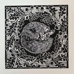 May include: A black and white linocut print depicting a curled hedgehog at the centre, framed by oak leaves and acorns. The print has a detailed, textured look, with the hedgehog's fur and the leaves' veins clearly visible. The style is reminiscent of woodcut prints.