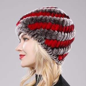 May include: A beanie hat featuring a textured, striped pattern of alternating bands of deep brown and vibrant red fur. The hat has a rounded, fitted shape that covers the crown of the head, showcasing a dense, soft, and plush appearance.