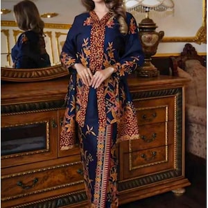 Puede incluir: Un conjunto azul marino con una blusa de manga larga y una falda a juego, ambas adornadas con un vibrante estampado floral en tonos naranja, rojo y amarillo. El atuendo se complementa con tacones blancos.