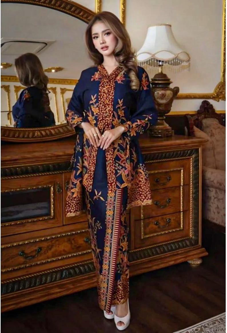 Puede incluir: Un conjunto azul marino con una blusa de manga larga y una falda a juego, ambas adornadas con un vibrante estampado floral en tonos naranja, rojo y amarillo. El atuendo se complementa con tacones blancos.