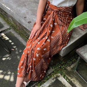 May include: A rust-colored skirt with a white geometric pattern. The skirt is tied at the waist and has a flowing silhouette.