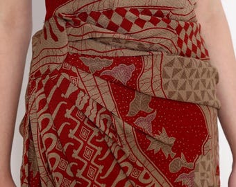May include: A red and tan patterned sarong with a detailed design. The fabric is wrapped around the waist, showcasing the intricate patterns and colors. The sarong features geometric shapes and floral motifs.