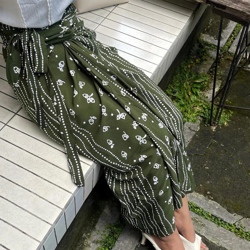 May include: A green wrap skirt with a white pattern of acorns and wavy lines. The skirt is tied at the waist with a matching fabric belt.