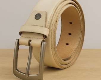 May include: A cream-colored leather belt with a silver-toned buckle. The belt is rolled up, showcasing its texture and stitching. The buckle is rectangular and the belt has a single decorative rivet near the buckle.