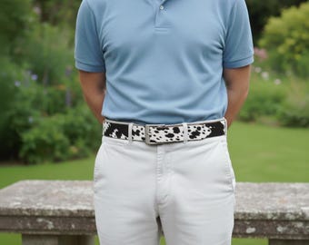 May include: A black and white cowhide belt with a silver buckle is worn over light-colored pants. The belt is approximately 1.5 inches wide. The person is wearing a light blue polo shirt.