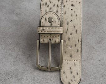 May include: A cream-colored belt with a speckled pattern and a silver-toned buckle. The belt has a rectangular buckle and a single belt loop. The belt is made of a textured material.