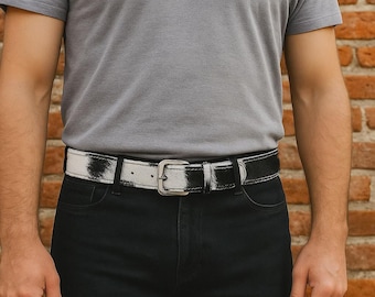 May include: A black and white cowhide belt with a silver-toned buckle. The belt is worn with black jeans and a gray t-shirt. The belt is approximately 1.5 inches wide.