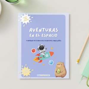 May include: A notebook titled "AVENTURAS EN EL ESPACIO" with a cartoon astronaut on a rocket ship. The cover is light blue with illustrations of planets and a bear holding an avocado. A pencil, keys, and a small notebook are also visible.