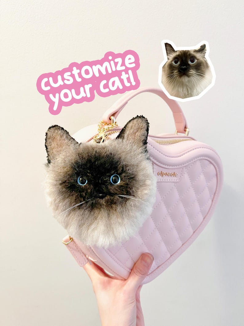 May include: A pink heart-shaped handbag with a plush cat face attached. The bag has a quilted pattern and a gold zip. The text "customize your cat!" is in a pink sticker. A cat sticker is also visible.