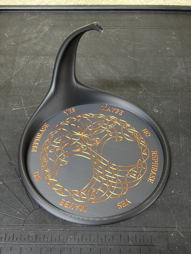 A black pendulum base features an intricate gold Tree of Life illustration surrounded by decision text against a workshop background.