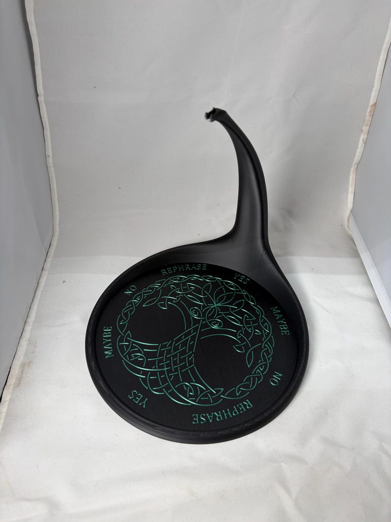 An empty black pendulum stand features a green Tree of Life symbol and divination options inside a white photographic backdrop.
