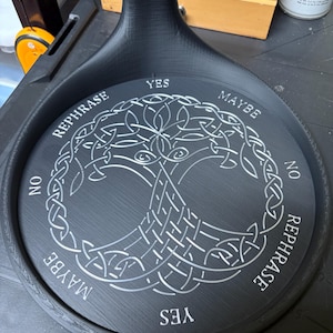 A black circular stand displays a silver Tree of Life carving alongside words like yes, no, maybe, and rephrase.