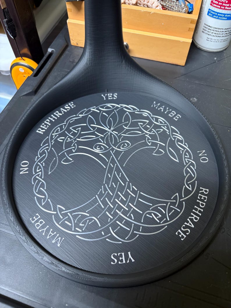 A black circular stand displays a silver Tree of Life carving alongside words like yes, no, maybe, and rephrase.