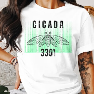 May include: White t-shirt featuring a green and black graphic of a cicada insect with the text "CICADA 3301" printed on the front.