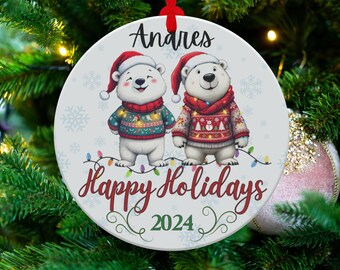 Puede incluir: Adorno navideño redondo con dos osos polares de dibujos animados con gorros de Papá Noel y jerséis. El adorno tiene el nombre "Andres" en la parte superior y el texto "Happy Holidays 2024" en la inferior. Colgando de un árbol de Navidad.