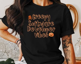 Może przedstawiać: Czarny T-shirt z pomarańczowym tekstem, który brzmi "Creepy Software Developer Vibes" z czaszką i skrzyżowanymi kośćmi oraz grafiką dyni.