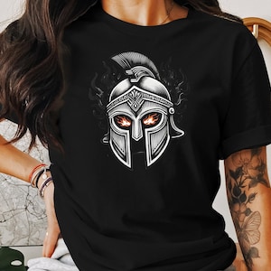 Puede incluir: Camiseta negra con un gráfico de un casco espartano plateado con llamas en las cuencas de los ojos.