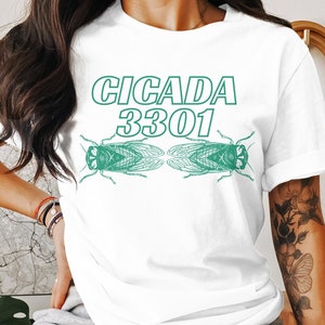 Puede incluir: Camiseta blanca con un gráfico verde de dos cigarras y el texto "CICADA 3301".
