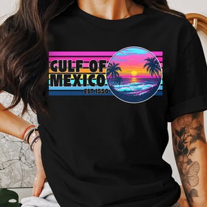 Könnte beinhalten: Schwarzes T-Shirt mit einem Retro-Grafikdesign, das einen Sonnenuntergang über dem Meer mit Palmen und dem Text "GULF OF MEXICO EST 1550" zeigt.