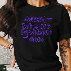 May include: Black t-shirt with purple text that reads "Wicked Software Developer Vibes" and a spider and bat graphic.