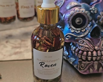 Può includere: Una bottiglia di vetro trasparente con contagocce bianco e oro, riempita di erbe e fiori secchi. L'etichetta recita "Rich Bitch Conjure's Raven Conjure Oil". Altre bottiglie sono sullo sfondo e un teschio decorativo è a destra.