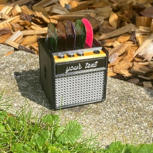 May include: A black and orange miniature guitar amplifier with a speaker grill and a slot for guitar picks. The amplifier has a label that says "your text".