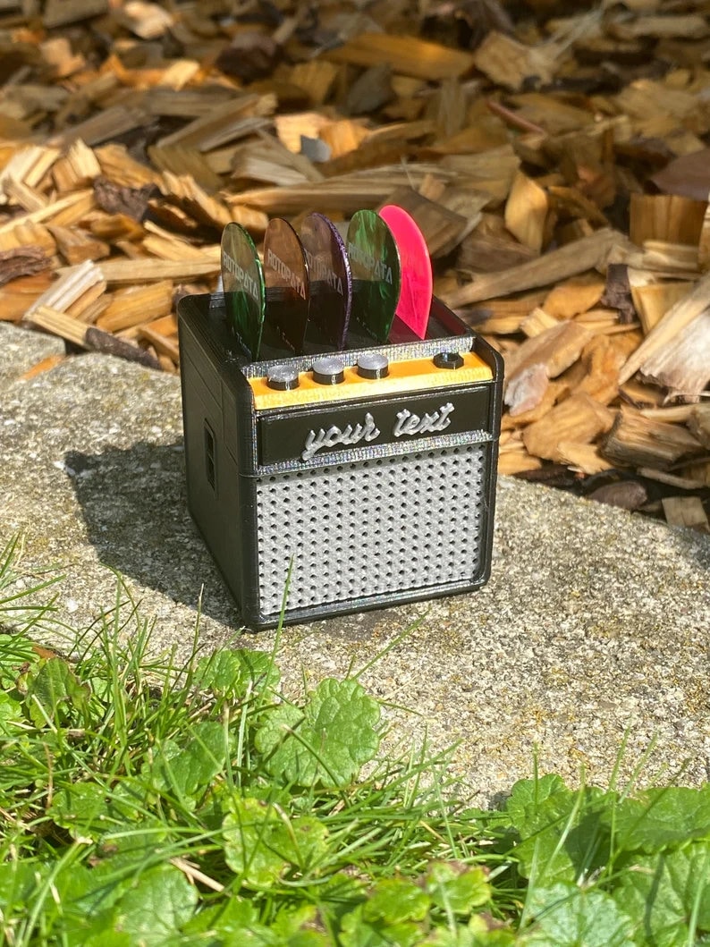 May include: A black and orange miniature guitar amplifier with a speaker grill and a slot for guitar picks. The amplifier has a label that says "your text".