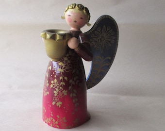 May include: A wooden angel figurine with a gold-colored cup. The angel has a red and gold floral patterned dress, blue wings with gold accents, and a light skin tone. The figurine is a decorative item.