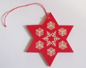 May include: A red, star-shaped Christmas ornament with a white snowflake design. The ornament has a red string for hanging. The star is made of a flat, solid material.