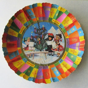 May include: A vintage Christmas paper plate with a colorful, patchwork-style border. The central image depicts children singing carols around a decorated Christmas tree. Gold accents and the text "Made in Western Germany" are visible.